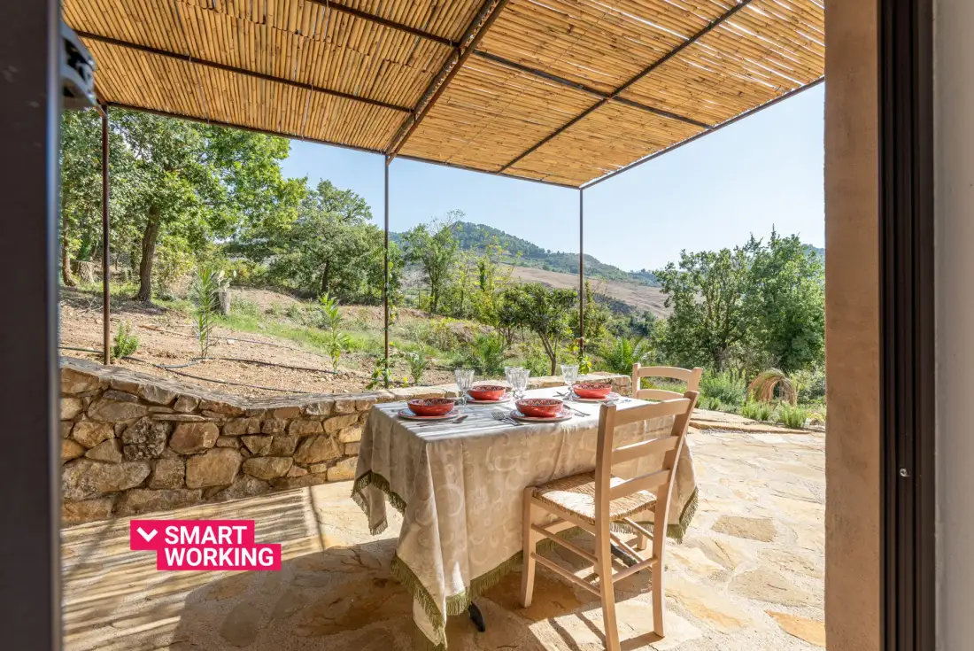 Una zona de comedor exterior cubierta con la mesa puesta y vistas a un paisaje verde.