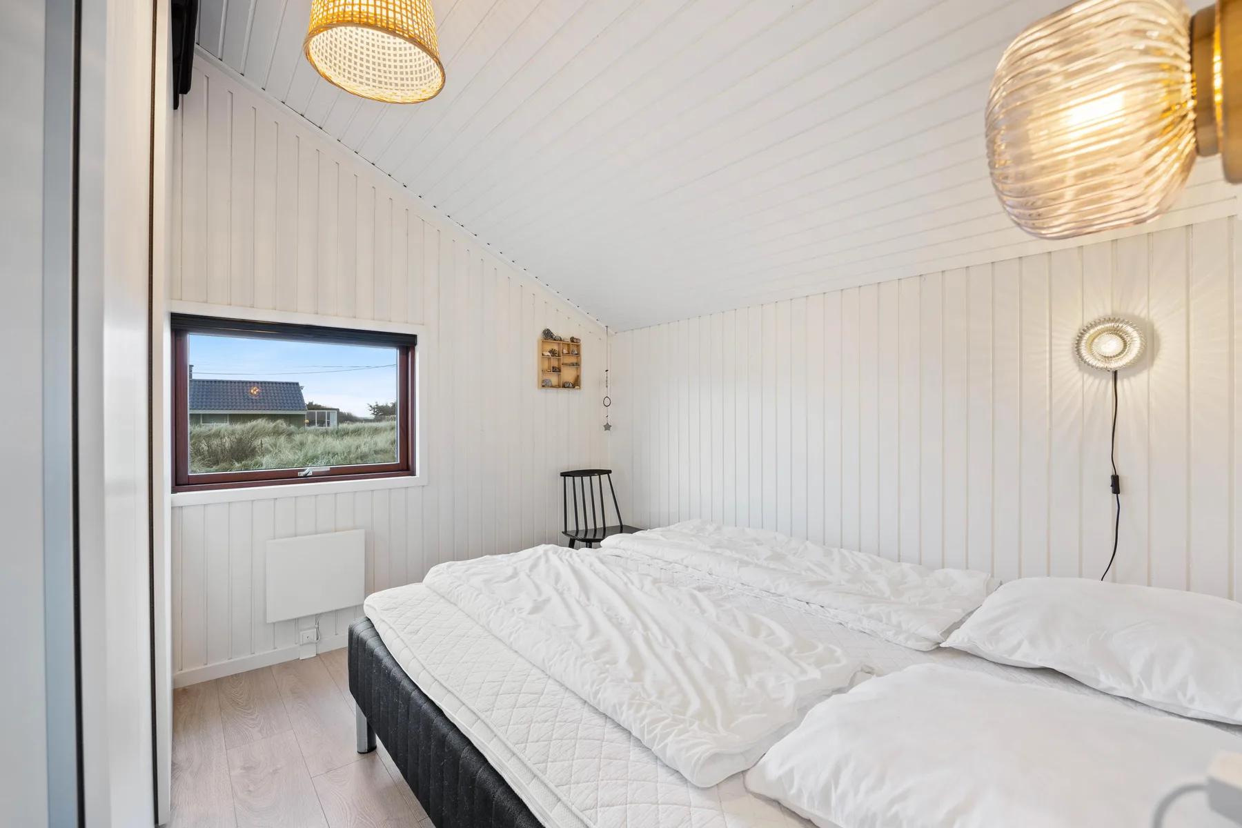 Un dormitorio luminoso con una cama junto a paredes blancas revestidas.