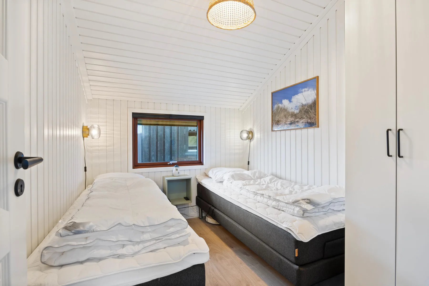 Un dormitorio luminoso con dos camas y una ventana al fondo.