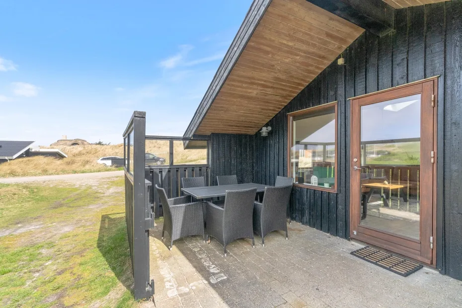 Un patio al aire libre con mesa de comedor y asientos junto a un edificio de fachada oscura.