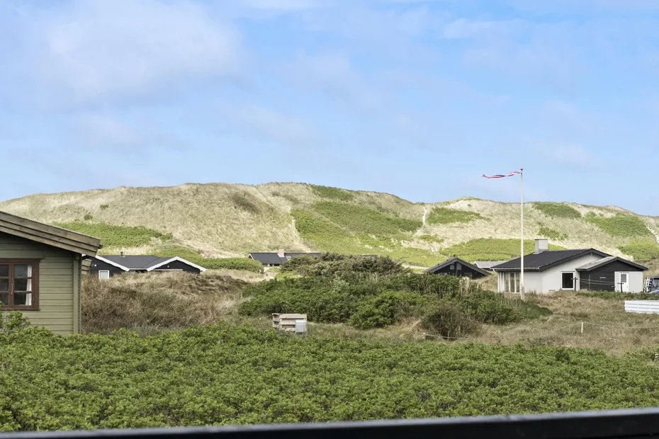 Paisaje de dunas con casas bajas y vegetación verde bajo un cielo azul.