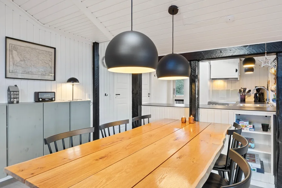 Un comedor luminoso tiene una larga mesa de madera bajo dos lámparas colgantes.