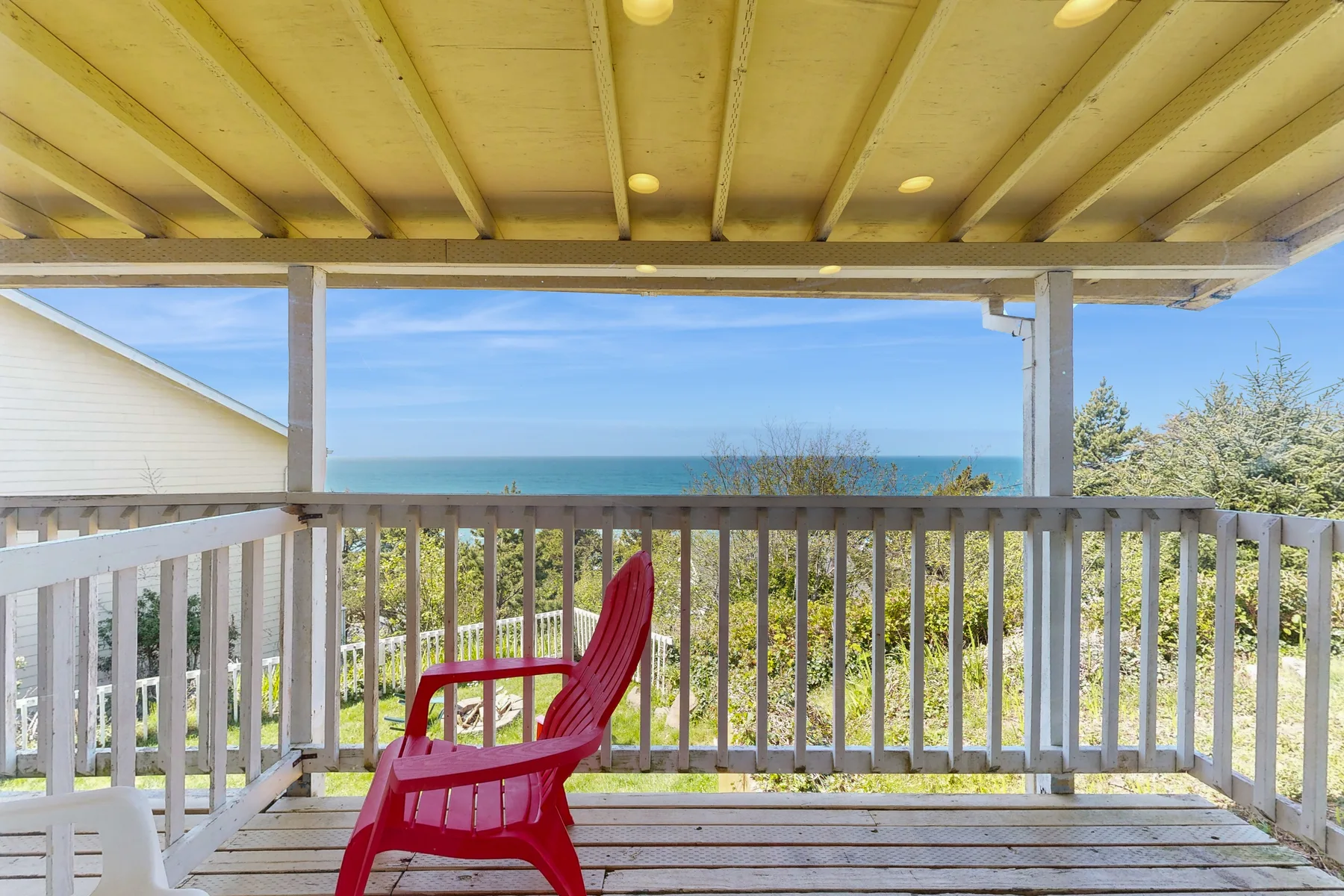 A covered outdoor deck overlooks the ocean, with a red chair by the railing.
