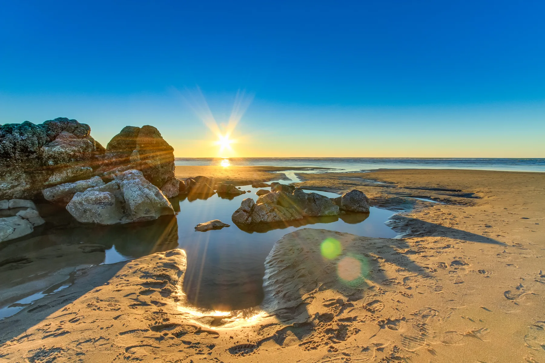 Una playa costera al atardecer, con rocas junto a charcas poco profundas.