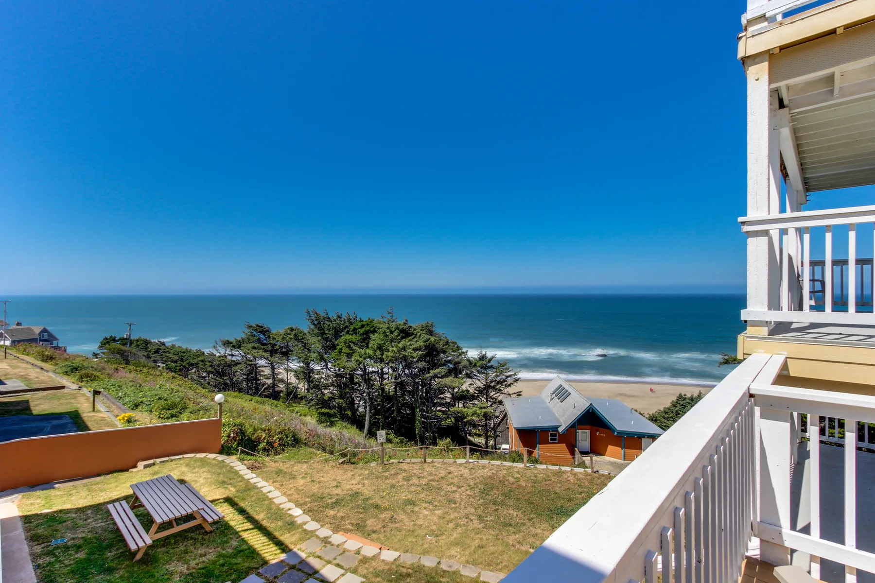 A balcony overlooks a grassy yard, coastal homes, and the ocean.