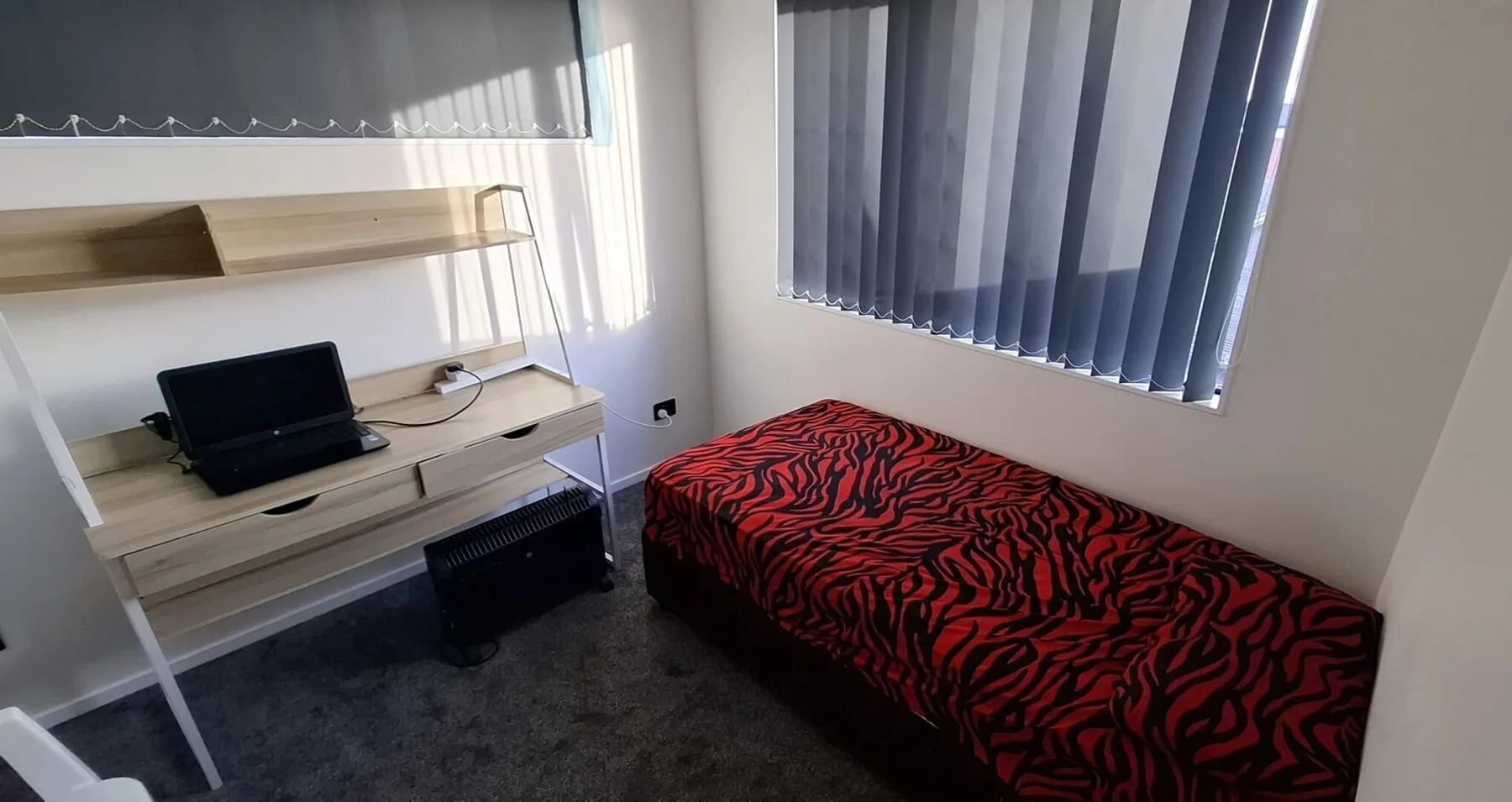 A bedroom with a single bed covered in a red-and-black patterned blanket.