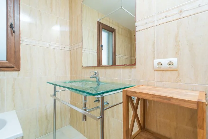 Un baño alicatado con un lavabo de vidrio y una mesa auxiliar de madera.