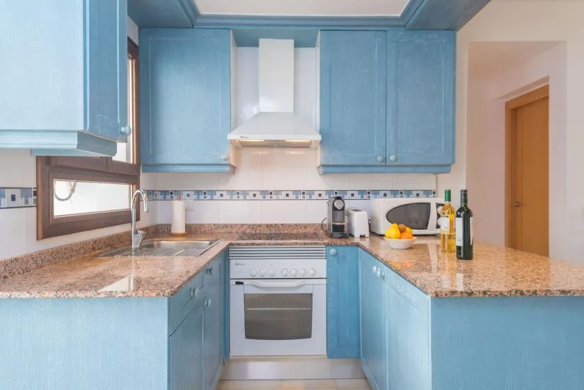 Una cocina azul con encimeras en forma de U, fregadero y horno integrado.