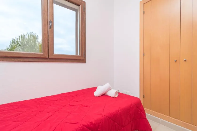 Un dormitorio con una cama cubierta con una colcha roja junto a una ventana.