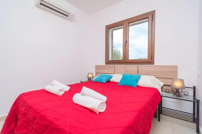 Dormitorio con una cama cubierta de rojo, cabecero de madera y ventana.