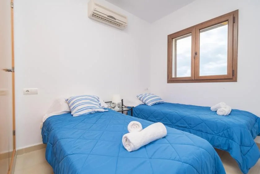 Un dormitorio con camas individuales, ropa de cama azul, almohadas a rayas y una ventana con marco de madera.