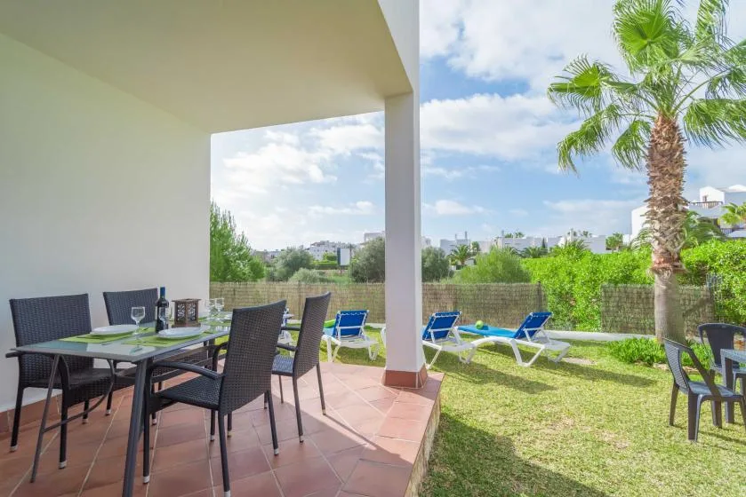 Un patio cubierto con asientos para comer se abre a un jardín con césped y tumbonas.