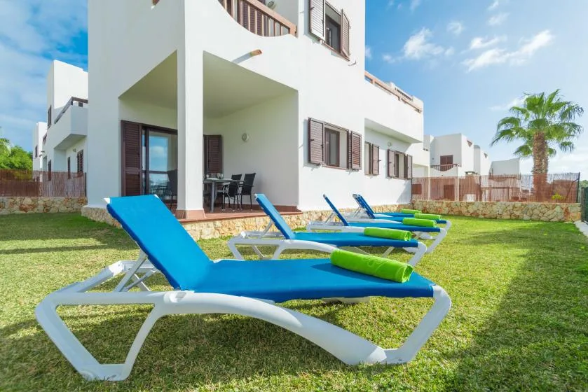 Outdoor poolside seating on a grassy lawn beside a white building.