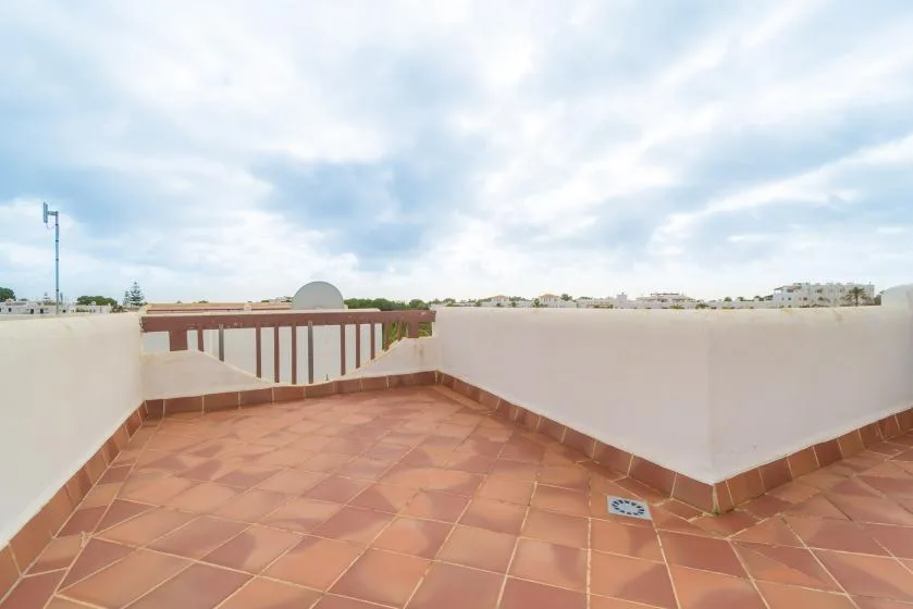 Una terraza abierta en la azotea con suelo de baldosas y un muro bajo.