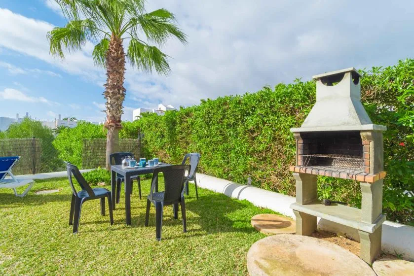 Un patio ajardinado con asientos al aire libre y una barbacoa junto a un seto.