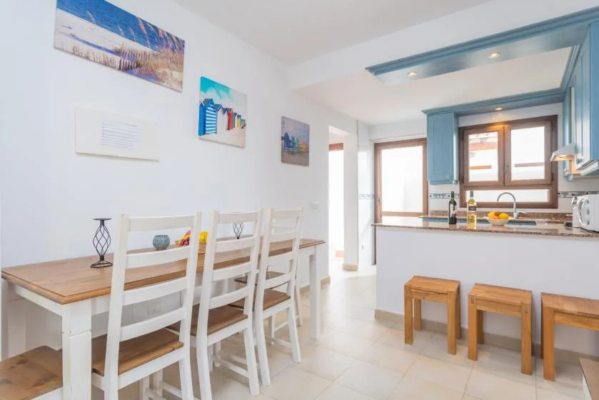 Una luminosa cocina con comedor, mesa, asientos blancos y una barra.