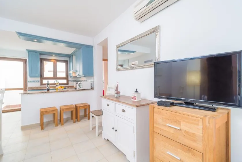 Una cocina luminosa con zona de comedor, una barra, taburetes y un televisor.