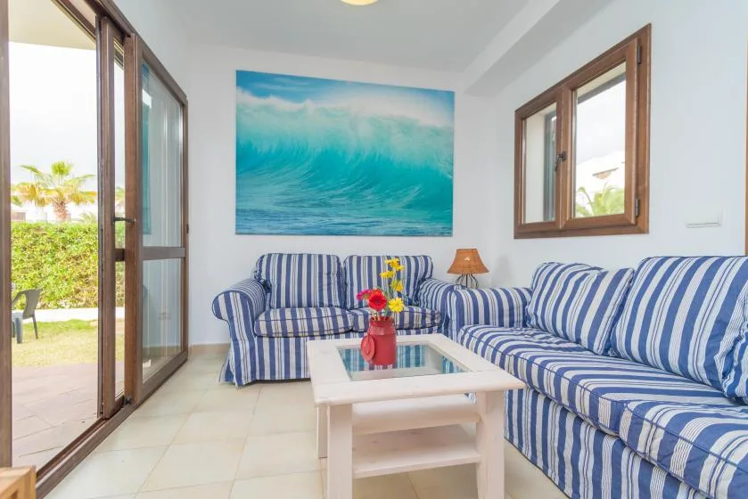 Una sala de estar con asientos a rayas azules y blancas y una mesa de centro bajo un cuadro de olas.