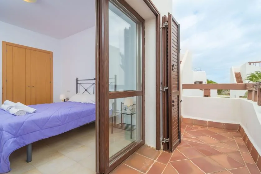 Un dormitorio se abre a un balcón de suelo embaldosado mediante una puerta de cristal.