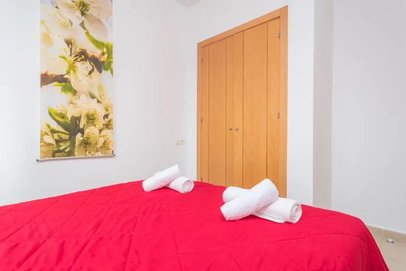 Dormitorio con una colcha roja, toallas dobladas y un armario de madera.