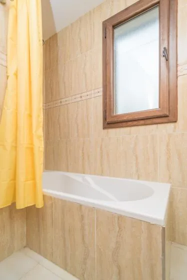 Un baño alicatado con bañera, cortina amarilla y ventana esmerilada.