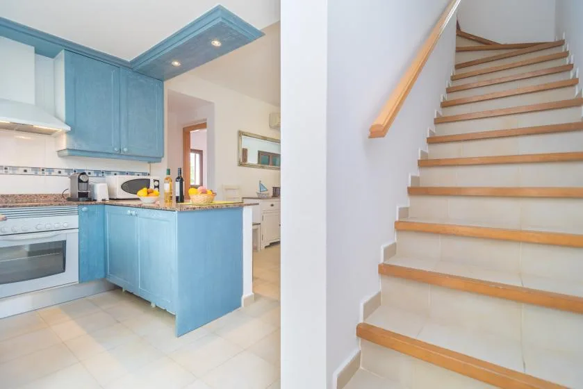 Una cocina azul con suelo de baldosas está junto a una escalera con pasamanos de madera.