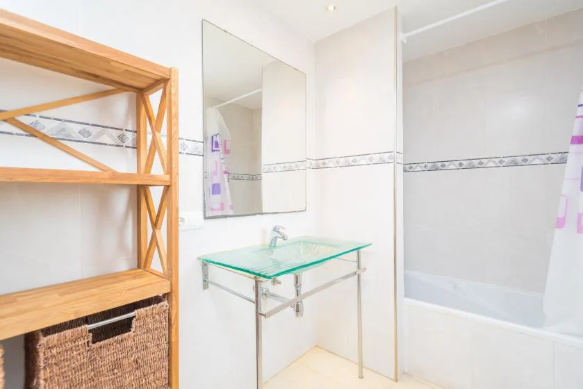 Un baño luminoso con lavabo de vidrio, espejo y bañera.