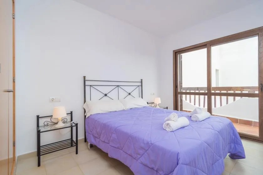 Un dormitorio con una colcha morada y una gran puerta corrediza de vidrio.