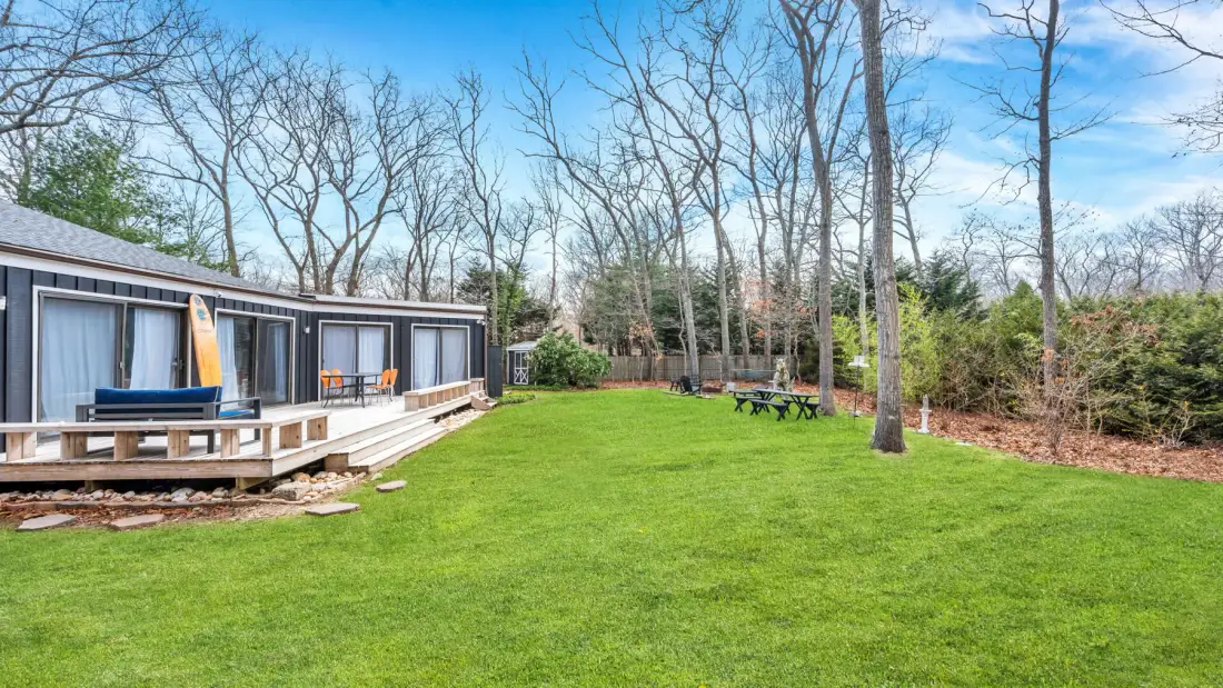 A grassy yard beside a low building, with trees and outdoor seating.