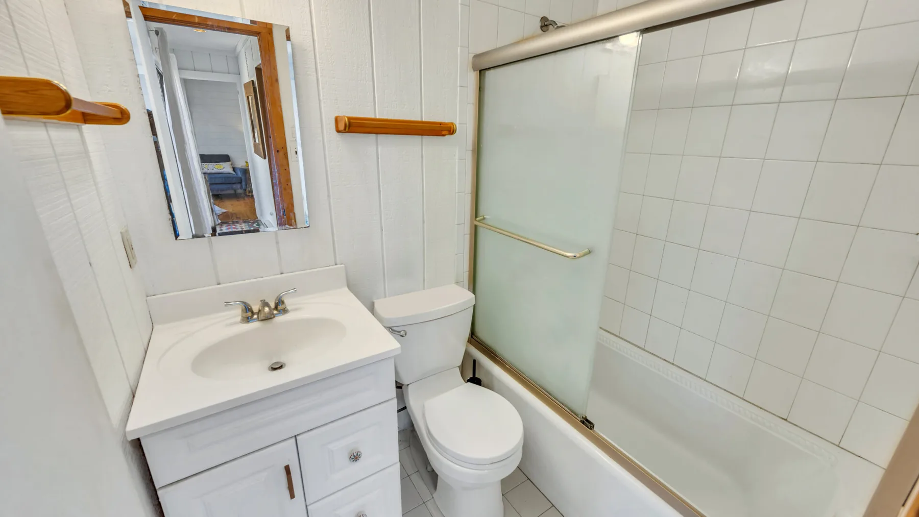 Un baño con azulejos, lavabo, inodoro y bañera detrás de un panel de vidrio corredizo.