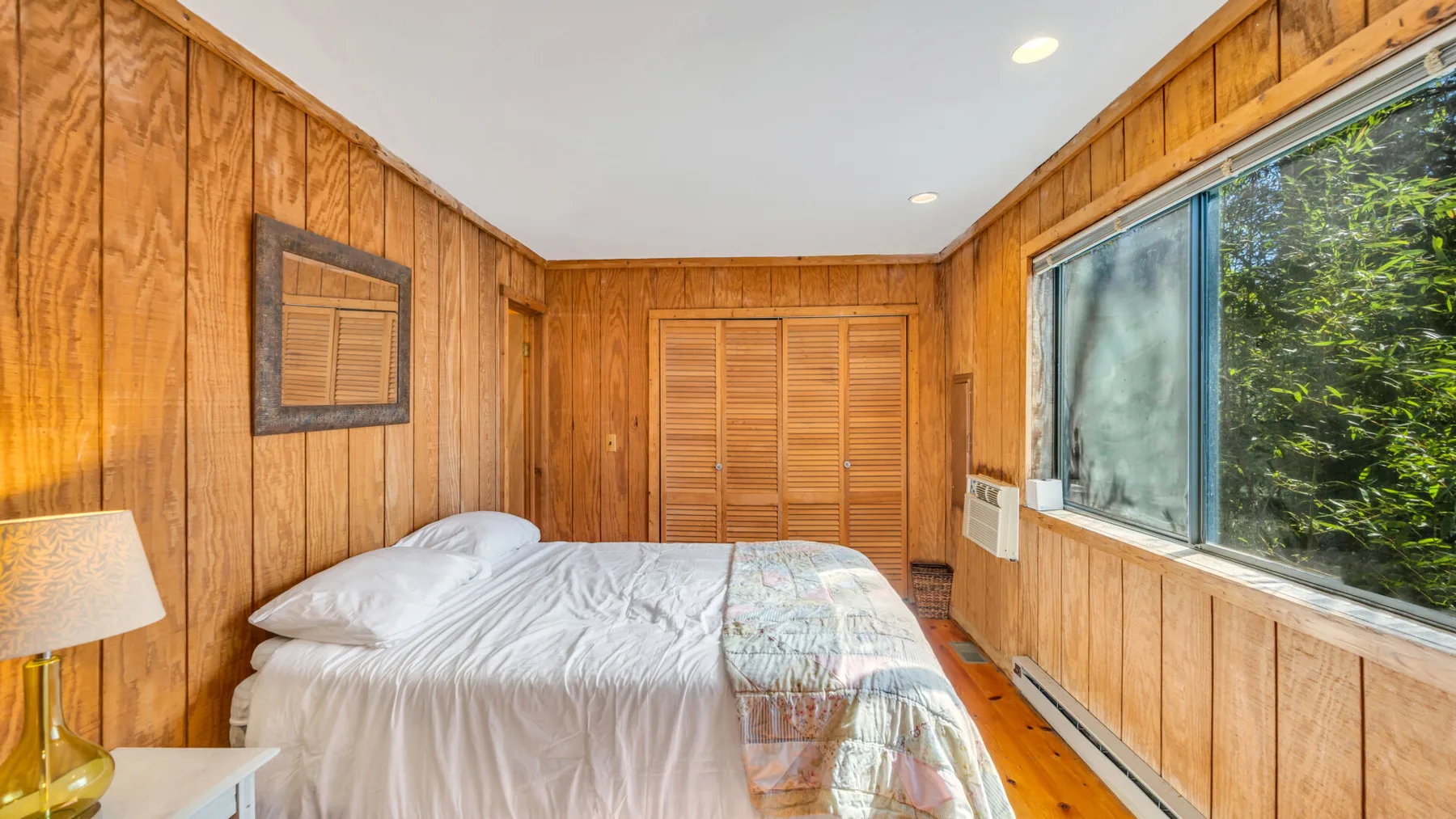 Un dormitorio con una cama junto a una ventana grande y paredes de madera.