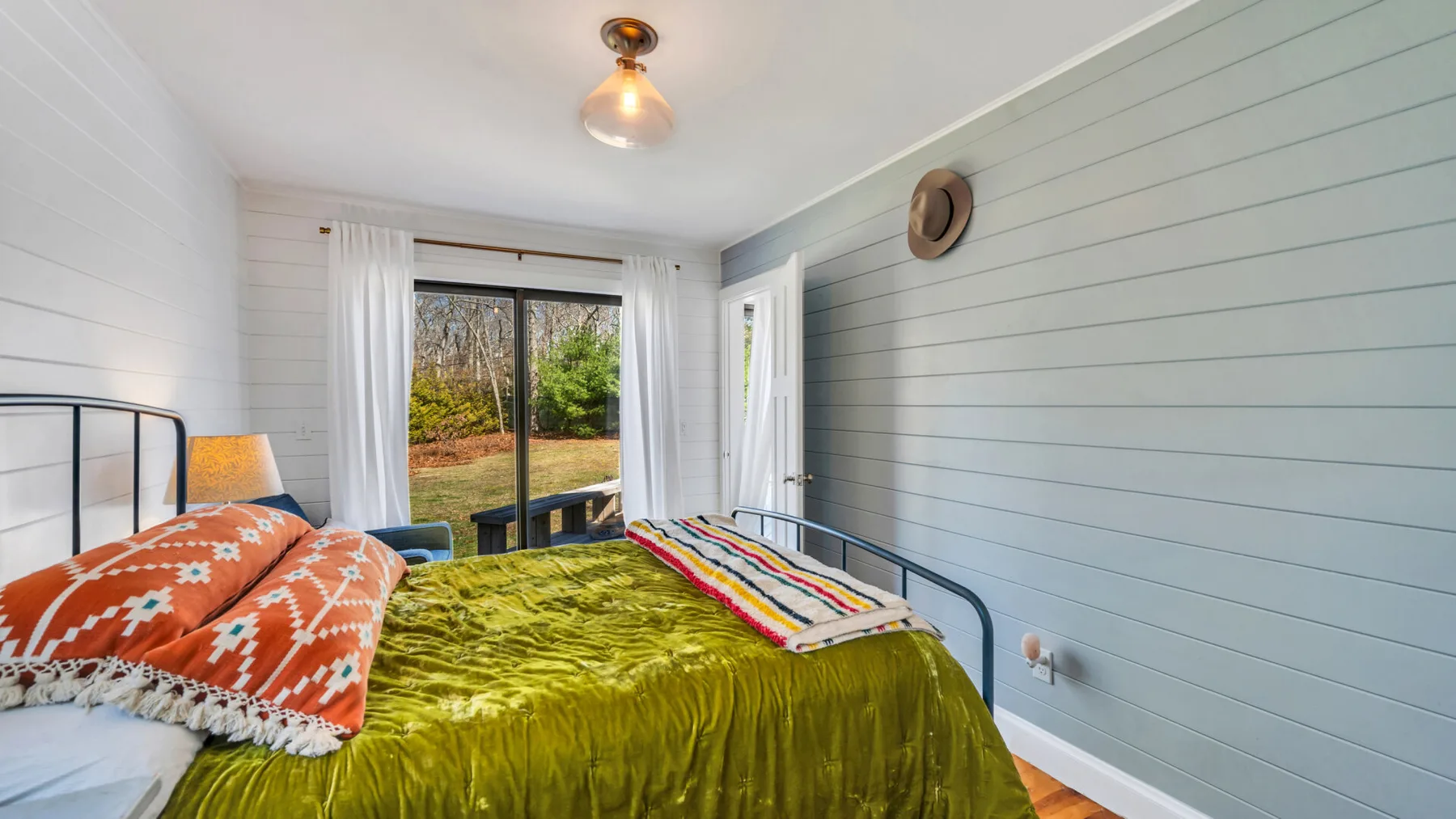 Un dormitorio con una colcha verde y ventanas con vista a un jardín.
