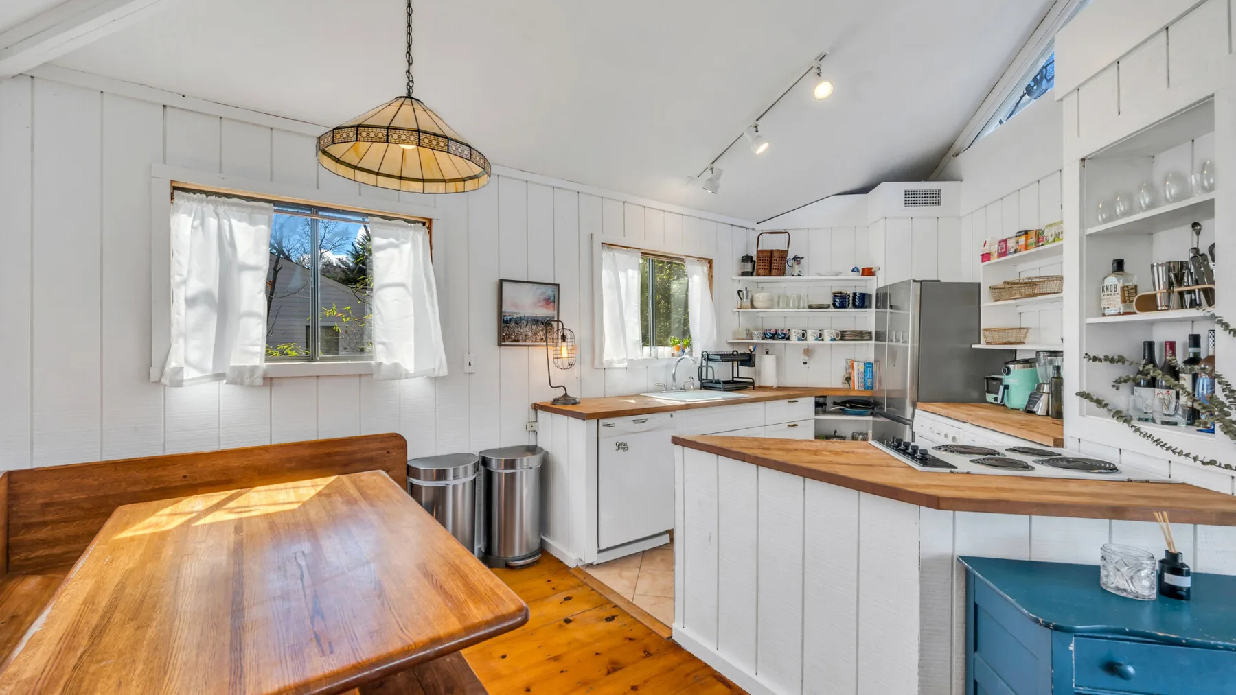 Una cocina luminosa con gabinetes blancos, encimeras de madera y una mesa de comedor.