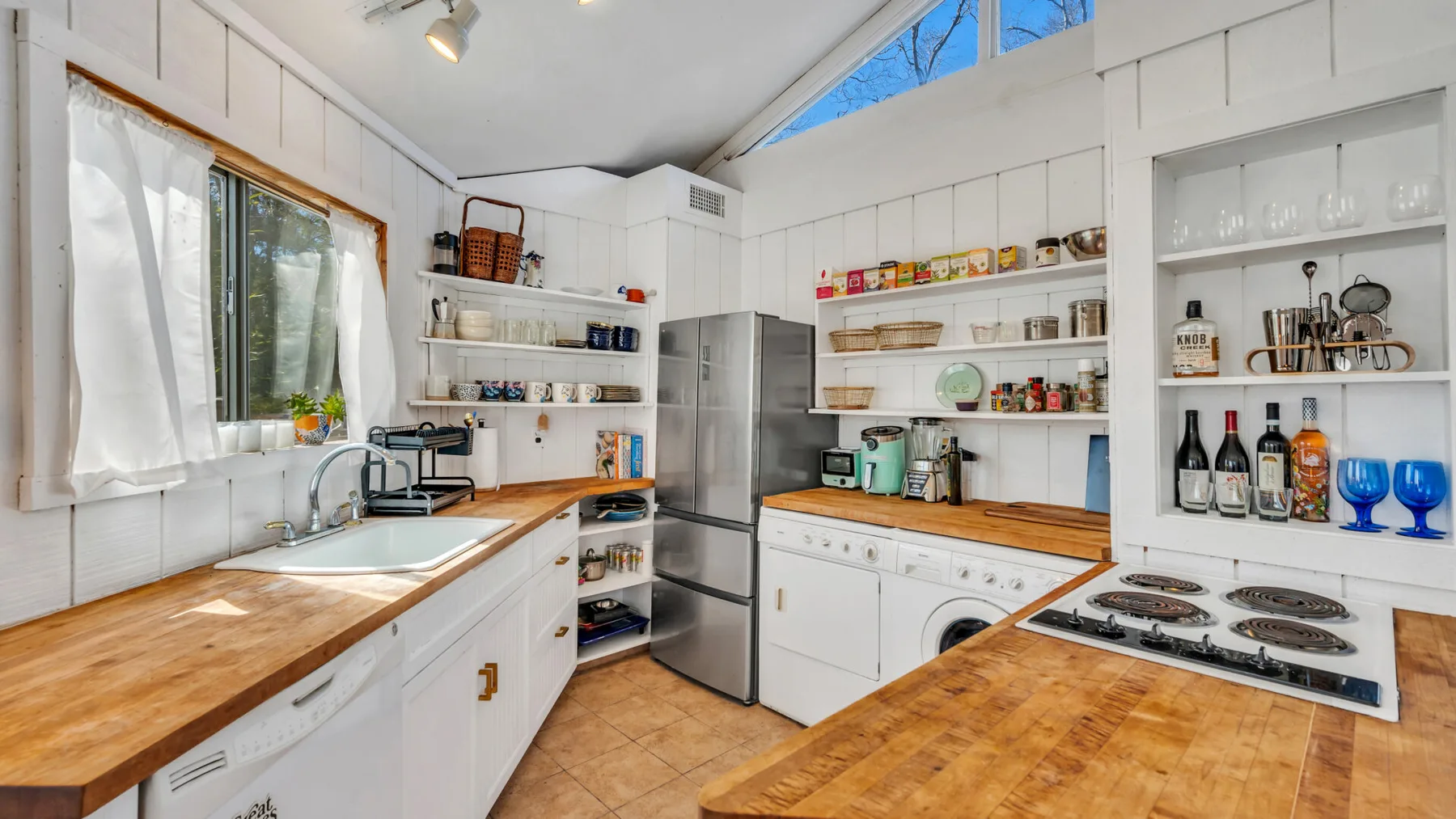Una cocina luminosa con encimeras de madera, armarios blancos y estantes abiertos.
