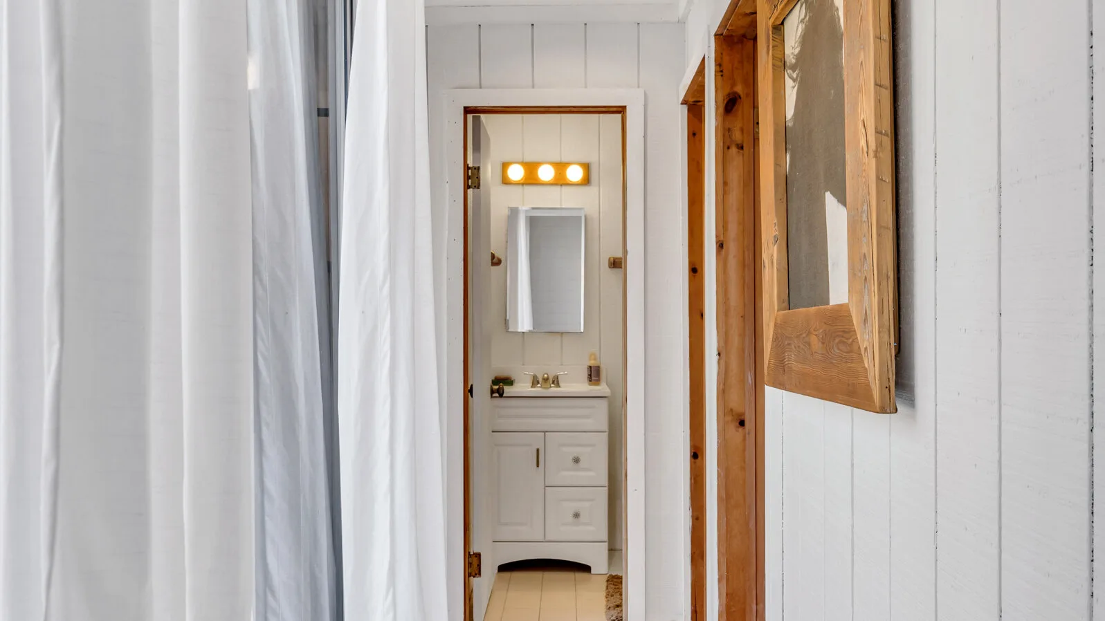 Un pasillo estrecho conduce a un lavabo de baño con espejo.