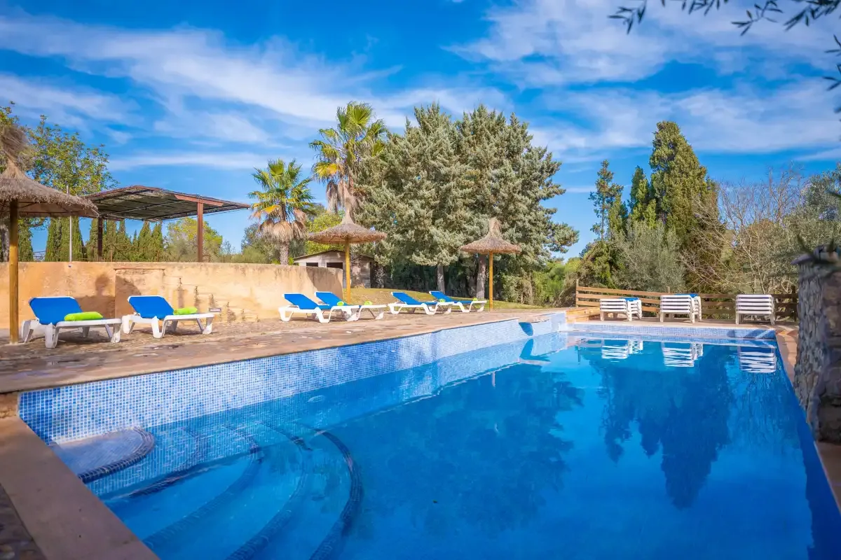 An outdoor swimming pool with blue loungers and thatched parasols beside the deck.
