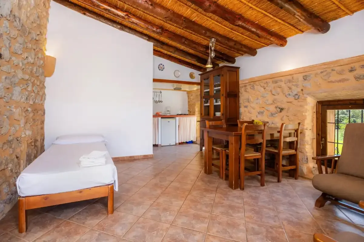 A rustic dining and living area with a wooden table beneath exposed ceiling beams.