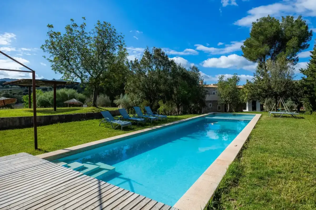 A long outdoor swimming pool sits beside a grassy yard and lounge seating.