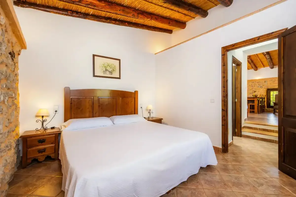A bedroom with a bed, wooden headboard, and exposed ceiling beams.