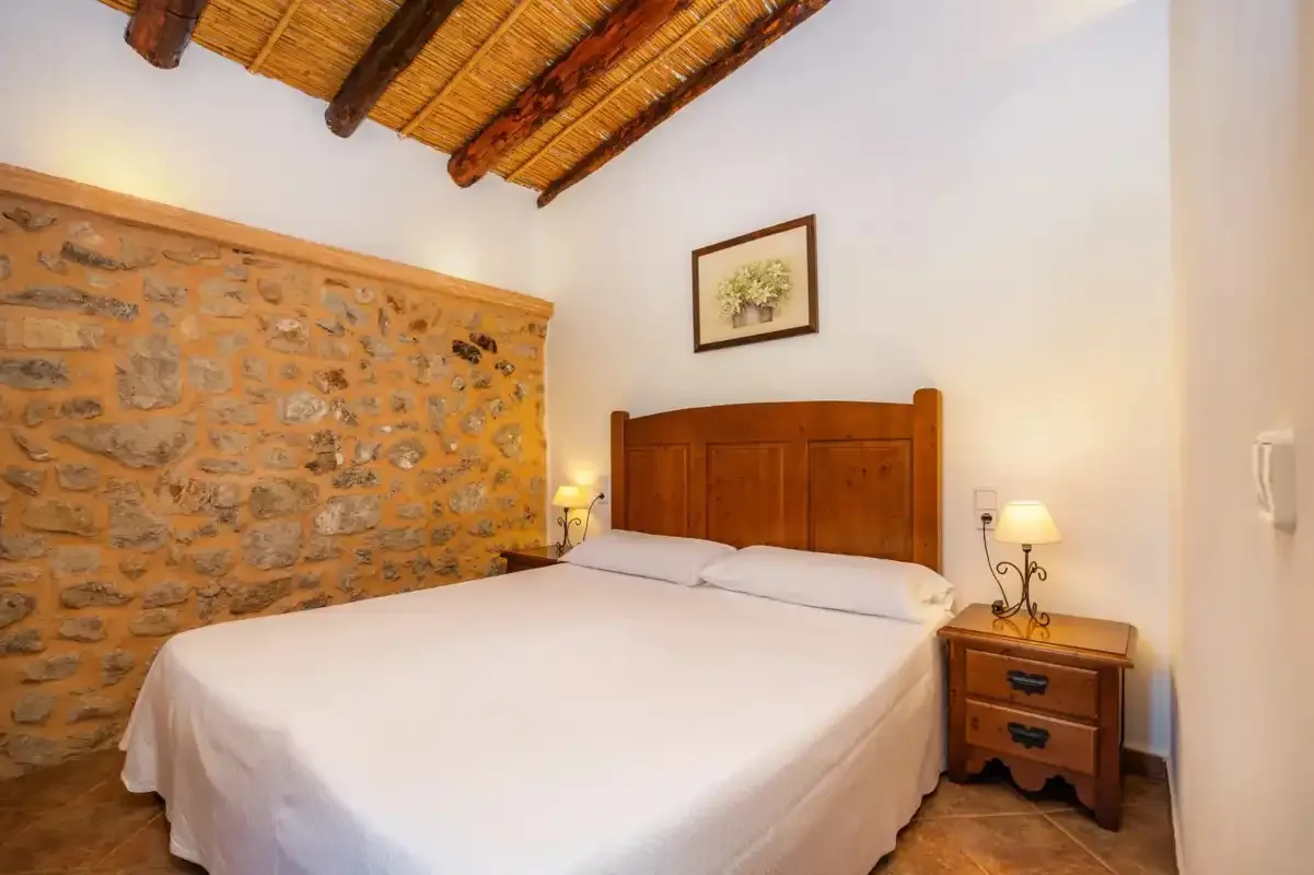 A bedroom with a bed, stone wall, and exposed wooden ceiling beams.
