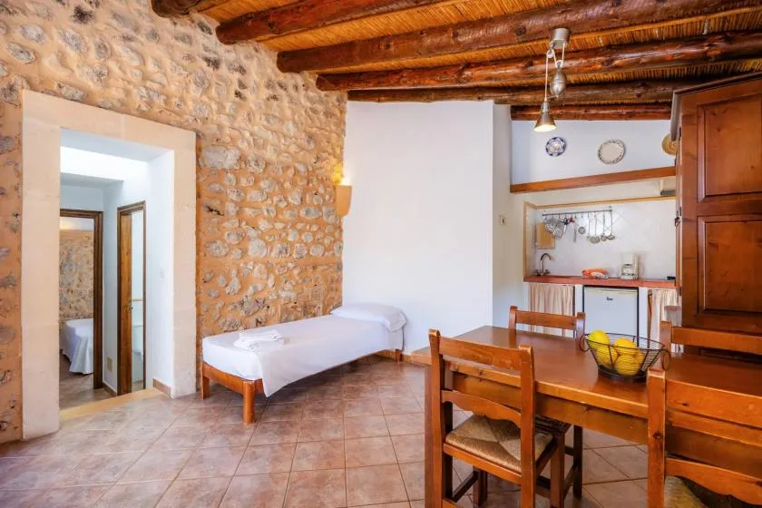 A rustic room with a single bed, wooden dining table, and exposed ceiling beams.