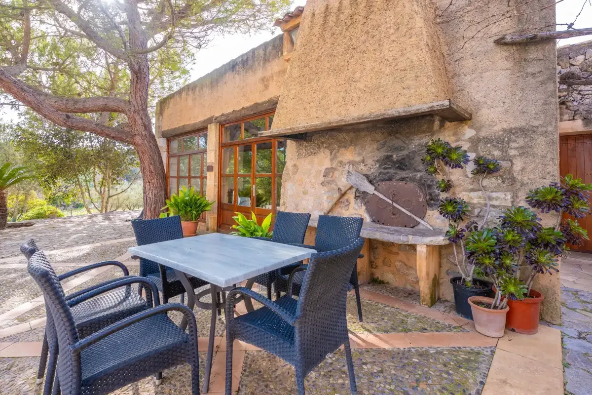 An outdoor dining area with dark woven seating beside a stone fireplace.