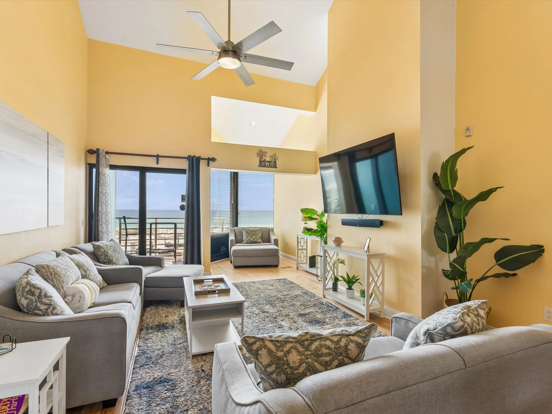 A living room with seating, a ceiling fan, and windows overlooking the water.