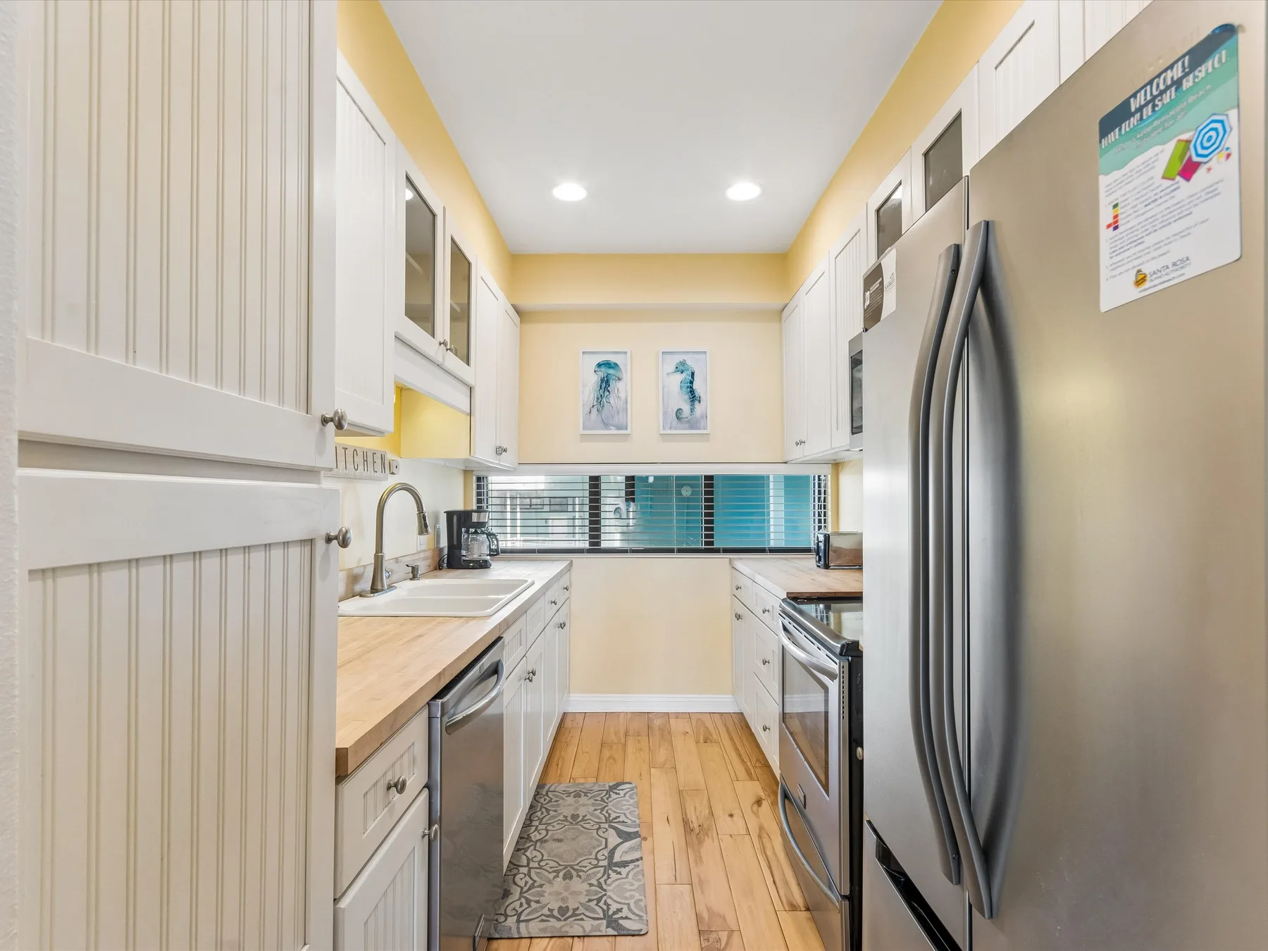 Una cocina luminosa con gabinetes blancos, electrodomésticos de acero inoxidable y piso de madera.