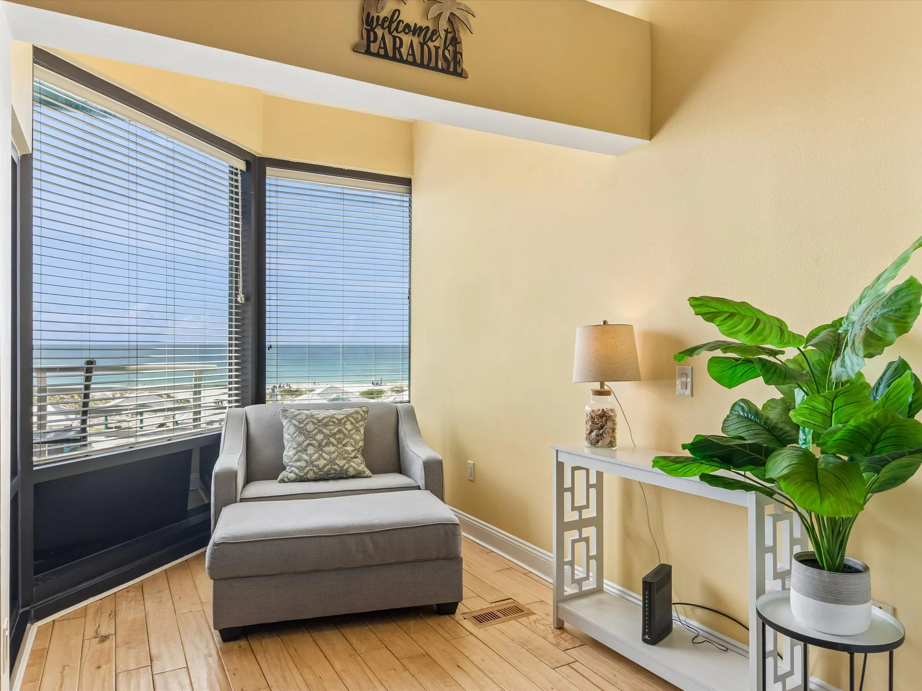 A bright living area has a lounge chair beside large windows overlooking the water.