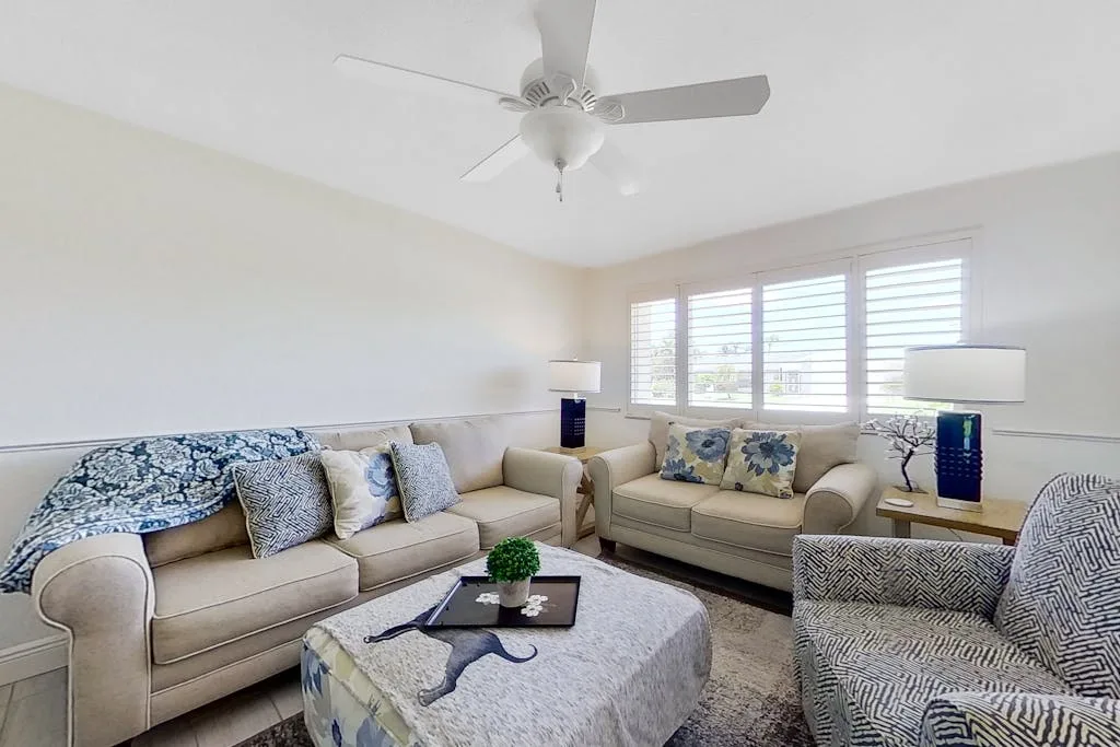 A bright living room with beige seating, patterned cushions, and wide windows.