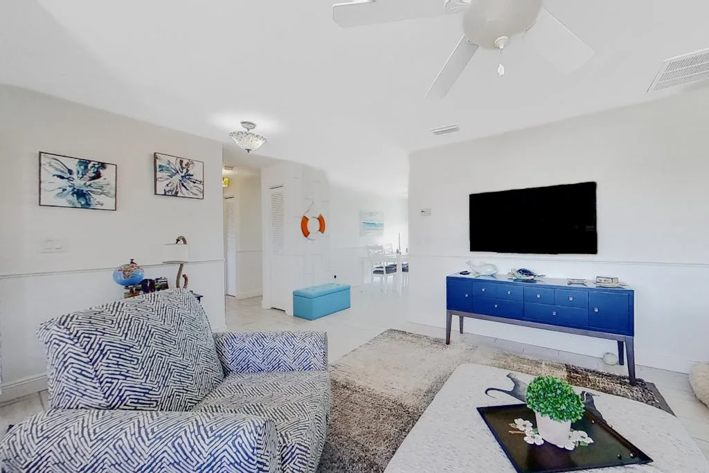 Una sala luminosa tiene asientos estampados, un aparador azul y un televisor en la pared.