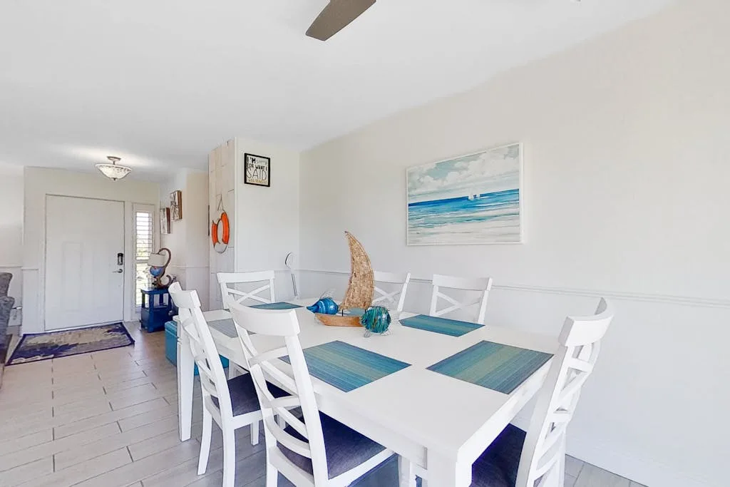 Comedor con una mesa blanca, sillas y arte mural de temática marina.