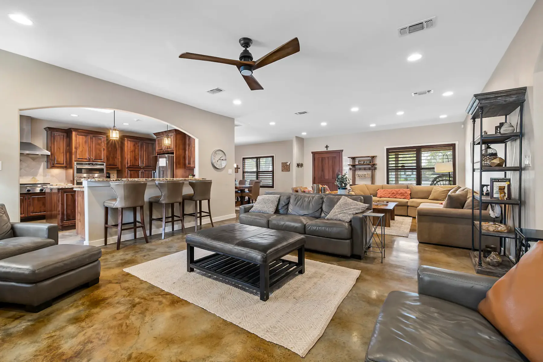 Open living area with seating, a kitchen counter, and a ceiling fan.