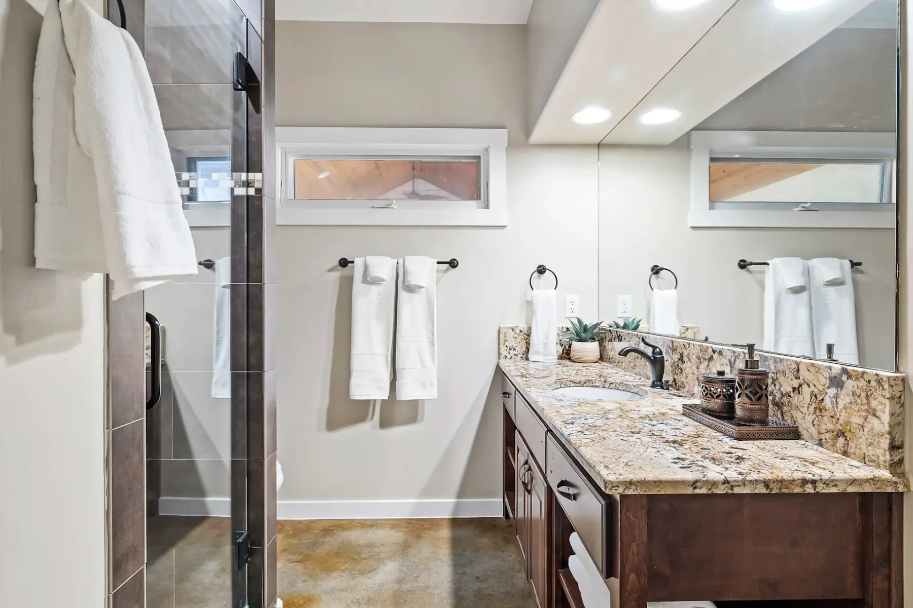 Un baño con un mueble de lavabo largo, un espejo grande y una ducha de vidrio.